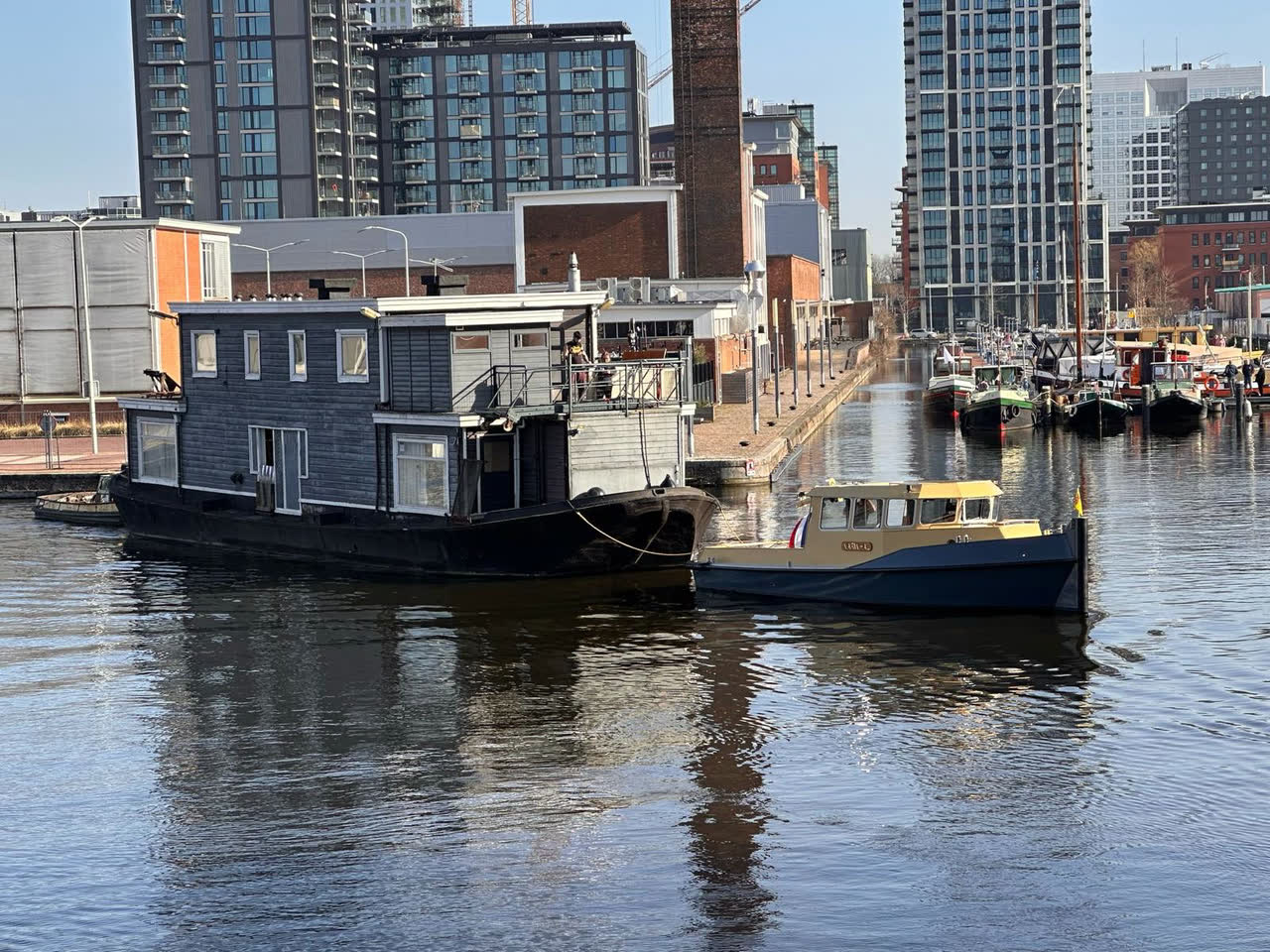 Sleepboot Narwhal met crèmekleurige opbouw langszij een woonschip in Amsterdam