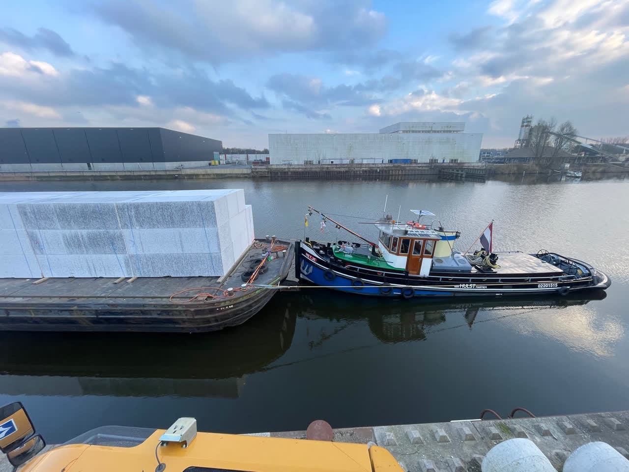 Ponton geladen met grote EPS drijflichamen, met de sleepboot langszij in een industriehaven