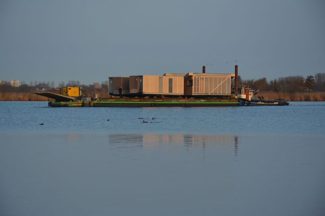 Ponton met prefab woonmodules wordt bij zonsondergang over het water gesleept