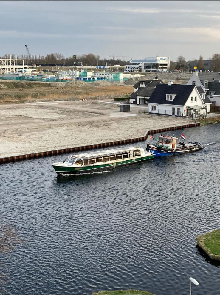 Rondvaartboot wordt door de sleepboot langs een nieuwbouwwijk aan het water gesleept