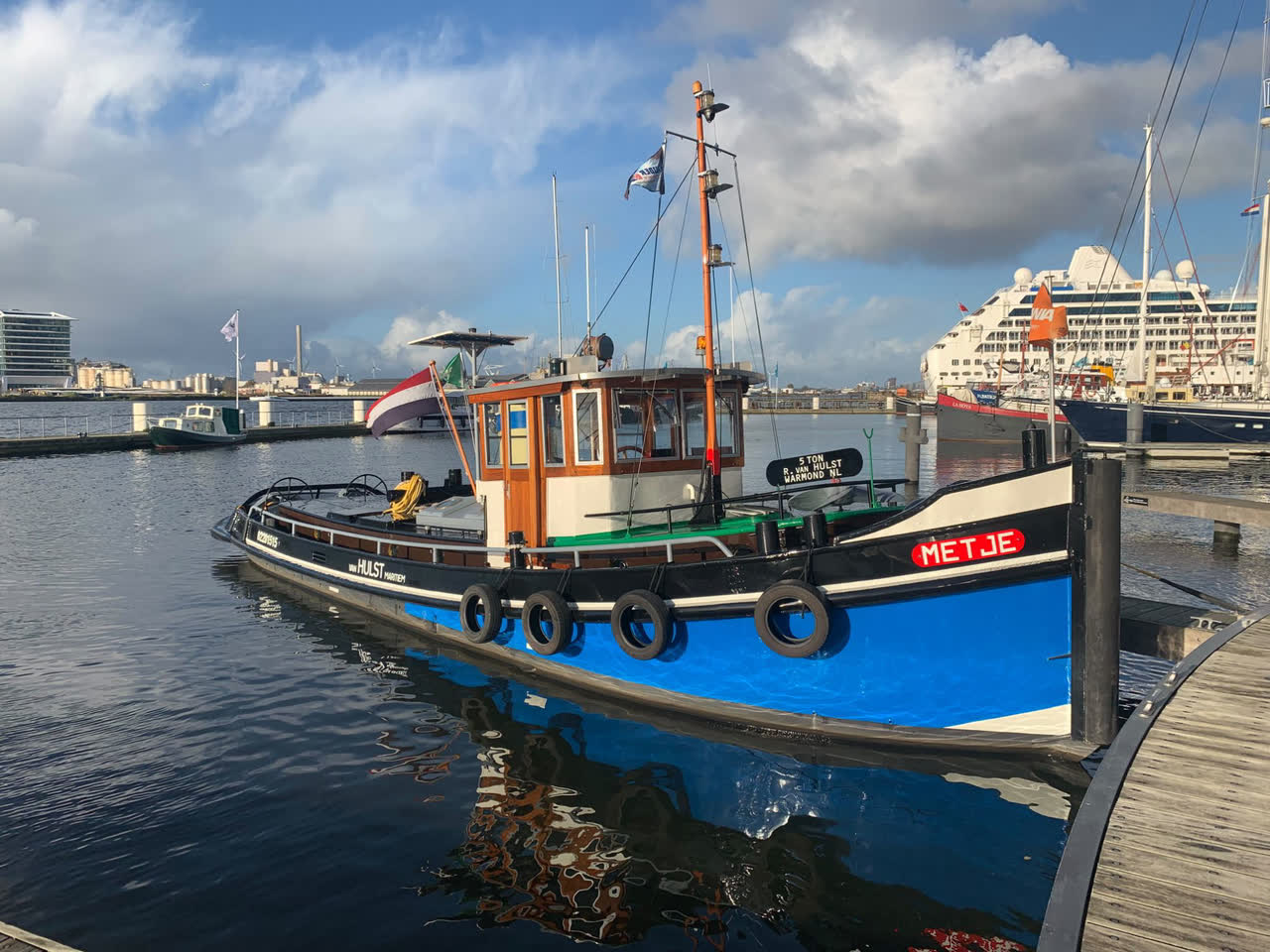 Sleepboot Metje afgemeerd aan een steiger in Amsterdam, met blauwe romp en houten stuurhut
