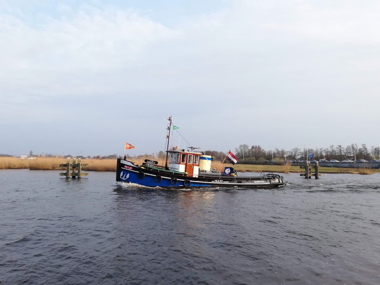 Sleepboot Metje vaart tussen remmingwerken door op open water bij Warmond